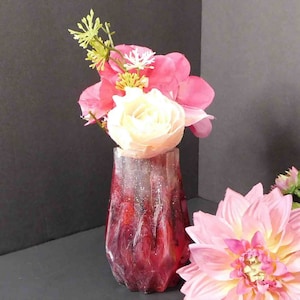 Op de afbeelding: Een rode en witte harsvaas met een geometrisch ontwerp bevat een boeket roze en witte bloemen.