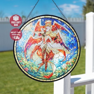 May include: A round stained glass window featuring a character playing a violin, with a hat and wings. The artwork uses a vibrant palette of red, orange, blue, and white, with a floral border. The window is framed in black and hangs from a chain.