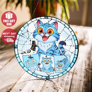 May include: Round stained glass window art featuring a blue cat with orange eyes and a bird wearing a top hat. The artwork includes three smaller blue cat illustrations. The window is framed with a blue border and a black chain for hanging.