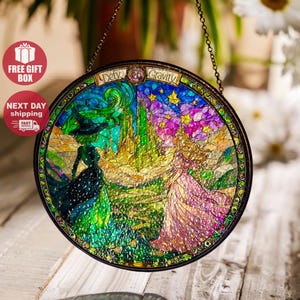 May include: Circular stained glass window art with a black metal frame. The artwork shows two figures, one in a black witch hat and gown, the other in a pink dress, with the text "Defy Gravity". The background features a green city and a starry sky.