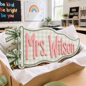 May include: A pennant-shaped wooden sign featuring a light green and white gingham pattern with the text Mrs. Wilson in raised pink lettering. The sign is decorated with two green and white gingham bows and green ribbon curls on the left side.
