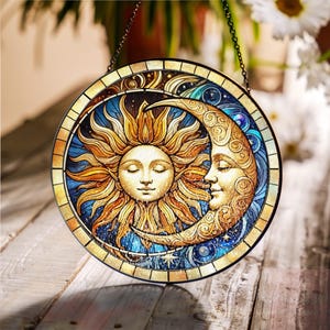 Könnte beinhalten: Ein Buntglasfenster mit einem Sonnen- und Mondmotiv in Blau, Gold und Weiß. Sonne und Mond sind mit Gesichtern dargestellt und von Sternen umgeben.