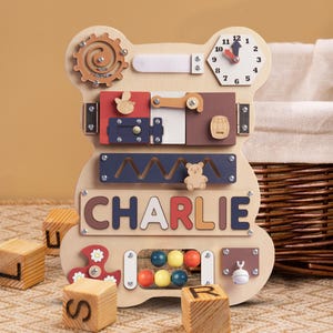 May include: Wooden toy bear activity board with a clock, a sliding door, a maze, a spinning wheel, a bead roller, a bell, and a nameplate that says "CHARLIE".