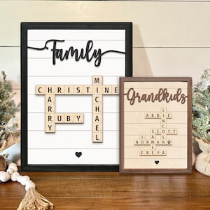 Könnte beinhalten: Zwei gerahmte Holzschilder mit den Wörtern "Family" und "Grandkids", die mit Scrabble-Steinen ausgeschrieben sind. Das Schild "Family" enthält die Namen Christine, Michael und Ruby. Das Schild "Grandkids" enthält die Namen Abbie, Scott, Norman und Freya.