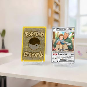 May include: Two collectible cards on clear stands. One card has "PokeDad" text and a yin-yang symbol. The other card says "Happy Father's Day 2026" and features an illustration of a grandfather and child reading.