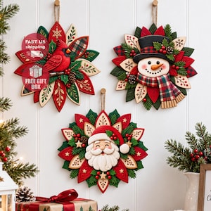 Könnte beinhalten: Drei kreisförmige Weihnachtswanddekorationen mit einem roten Kardinal, einem Schneemann mit schwarzem Zylinder und kariertem Schal sowie dem Weihnachtsmann, umgeben von geschichteten roten und grünen Blättern und Beeren.