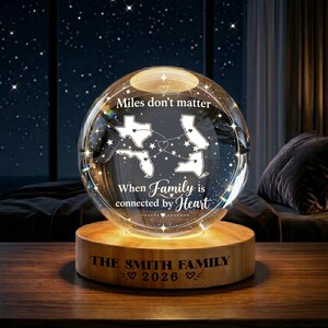 May include: A clear glass sphere lamp on a cylindrical wooden base. The sphere features white etched outlines of Texas, California, Florida, and New York connected by dotted lines, with the text "Miles don't matter When Family is connected by Heart". The base reads "THE SMITH FAMILY 2026".