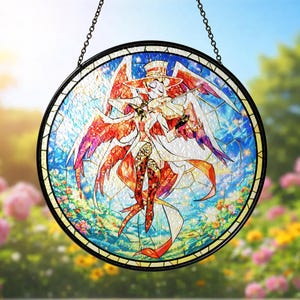 May include: Round stained glass panel featuring a whimsical angel playing a violin. The angel has red and white wings, a top hat, and a flowing white coat. The background is a mix of blue, white, and floral patterns, with a black metal frame and chain.