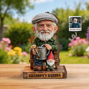 Könnte beinhalten: Eine skurrile Gartenfigur mit einem lächelnden älteren Mann mit weißem Bart, der ein kariertes Hemd und eine Mütze trägt und eine Gießkanne hält. Ein kleiner Zwerg sitzt neben ihm. Auf dem Sockel steht "Grandpa's Garden".