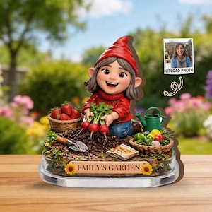 Könnte beinhalten: Gartenzwerg-Figur mit rotem Hut und Pullover, der Radieschen hält. Körbe mit Erdbeeren und Gemüse umgeben den Zwerg. Auf der Basis steht "EMILY'S GARDEN". Ein Foto ist im Hintergrund.