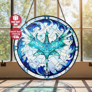 May include: Round stained glass window art featuring a teal and blue avian creature design. The artwork is framed in black and hangs from a chain. The design includes wave and star patterns.