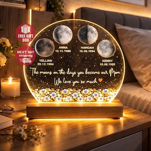 May include: A personalized moon phase night light with a wooden base. The clear acrylic disc features four moon phases, names, and dates. Text reads "The moons on the days you became our Mom. We love you so much."
