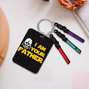 May include: A black keychain with the text "I AM YOUR FATHER" and a Darth Vader graphic. Attached are three lightsaber-shaped keychains in red, teal, and purple, each with a name: MIA, LISA, and RAMBO.