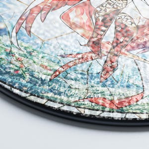 May include: Round decorative plate with a mosaic design featuring red and white abstract shapes against a blue and green background. The plate has a black rim and a glossy finish, suitable for home decor.