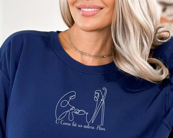 May include: A navy blue sweatshirt with a white outline of the nativity scene and the text "Come let us adore Him".