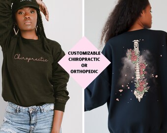 Op de afbeelding: Twee zwarte sweatshirts met verschillende ontwerpen. Een sweatshirt heeft het woord "Chiropractic" in roze schrift. Het andere sweatshirt heeft een afbeelding van een wervelkolom met bloemen erop. De tekst "CUSTOMIZABLE CHIROPRACTIC OR ORTHOPEDIC" is in roze op een witte achtergrond geschreven.