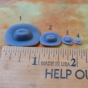 May include: Four gray felt cowboy hats of different sizes, lined up from largest to smallest, with the numbers 1 through 4 above them. The hats are on a wooden ruler marked "Made in USA" and "Help Our..."