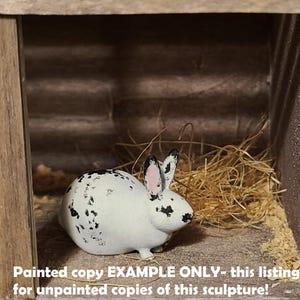 May include: A black and white painted rabbit figurine in a wooden hutch. The rabbit is sitting in a bed of straw. "Painted copy EXAMPLE ONLY - this listing is for unpainted copies of this sculpture!" is written below the rabbit.