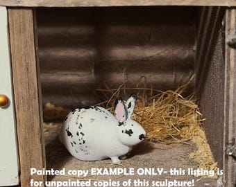 May include: A black and white painted rabbit figurine in a wooden hutch. The rabbit is sitting in a bed of straw. "Painted copy EXAMPLE ONLY - this listing is for unpainted copies of this sculpture!" is written below the rabbit.