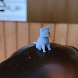 Op de afbeelding: Een klein, lichtblauw 3D-geprint beeldje van een kat die op een donkerbruin oppervlak zit.