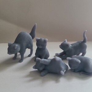 Op de afbeelding: Vijf grijze 3D-geprinte kattenfiguren. De katten staan in verschillende poses, waaronder zittend, liggend en staand.