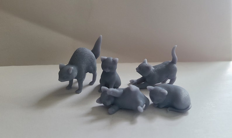 Op de afbeelding: Vijf grijze 3D-geprinte kattenfiguren. De katten staan in verschillende poses, waaronder zittend, liggend en staand.