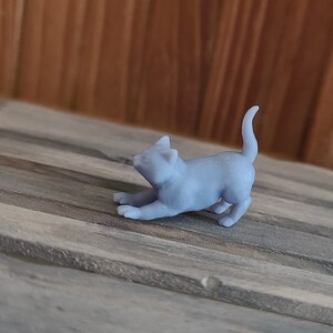 Op de afbeelding: Een klein, grijs, 3D-geprint beeldje van een kat in een speelse pose. De kat ligt op zijn buik met zijn voorpoten gestrekt en zijn staart opgerold.