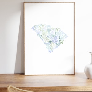 May include: A framed print of a stylized outline of the state of South Carolina, filled with blue, green, and yellow abstract shapes.