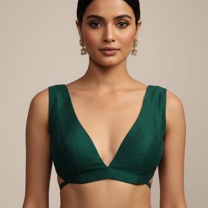 May include: A sleeveless, emerald green top with a deep V-neckline. The top features a tailored fit and a cutout design on the sides. The model is wearing gold earrings.