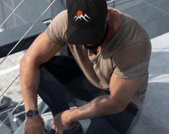 May include: A black baseball cap with an embroidered design of a mountain range and a setting sun. The sun is orange and the mountains are white.