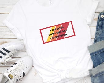 Op de afbeelding: Wit T-shirt met een rode, oranje en gele afbeelding met de tekst "TOYOTA OFF-ROAD LEGENDS".