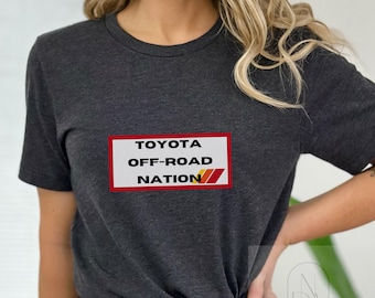 Op de afbeelding: Een donkergrijs T-shirt met een rechthoekige grafische afbeelding in rood, wit en oranje met de tekst "TOYOTA OFF-ROAD NATION".