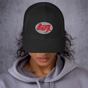 May include: Black trucker hat with a gray oval patch featuring the red kanji character "侍" (Samurai) in a stylized font.