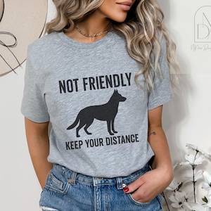 Op de afbeelding: Grijs T-shirt met een zwart silhouet van een Duitse herder en de tekst "Not Friendly Keep Your Distance".