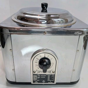 May include: A vintage chrome Super Electric deep fryer with a black knob and temperature dial. The dial indicates temperatures up to 350 degrees Fahrenheit. The fryer has a lid with a black handle and a list of cooking times.