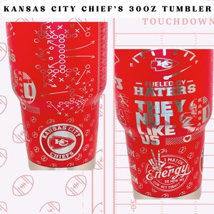 May include: A red 30 ounce tumbler featuring a Kansas City Chiefs logo and the words "Fueled by Haters They Not Like Us". The tumbler also has a football play diagram and the words "Touchdown" printed on it.