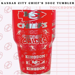 May include: Red stainless steel tumbler with a silver Kansas City Chiefs logo and the words "KANSAS CITY CHIEF'S 300Z TUMBLER" and "TOUCHDOWN".