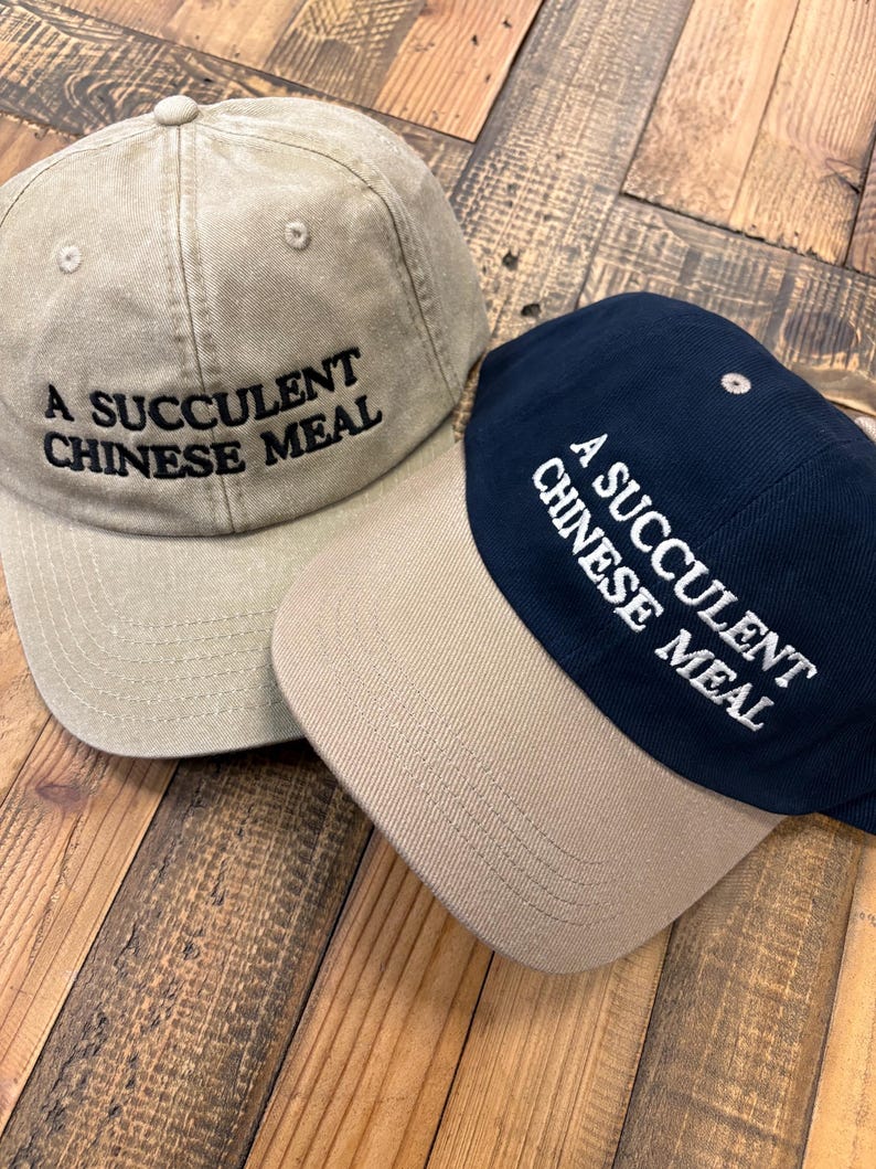 Puede incluir: Dos gorras de b&eacute;isbol con el texto "A succulent Chinese meal" bordado en la parte delantera. Una gorra es beige y la otra es azul marino.