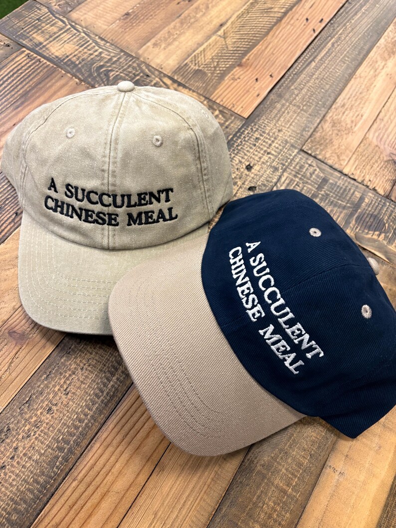 Puede incluir: Dos gorras de b&eacute;isbol con el texto "A succulent Chinese meal" bordado en la parte delantera. Una gorra es beige con una visera beige y la otra es azul marino con una visera beige.