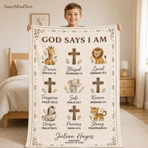 Op de afbeelding: Een crèmekleurige fleecedeken met de tekst GOD SAYS I AM, illustraties van een giraf, leeuw, olifant, zebra en luipaard, drie bruine kruisen en religieuze verzen. De naam Julian Hayes en August 15, 2026 staan onderaan gedrukt.