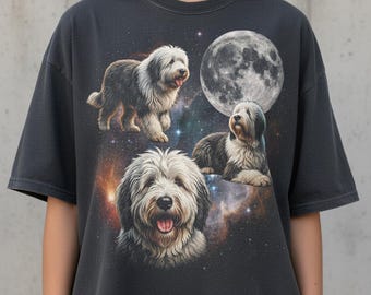 May include: Dark grey t-shirt with a graphic of a Bearded Collie dog, a full moon, and a starry galaxy. The dog is shown in three poses. The shirt is made of a soft material.
