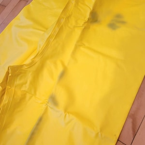 May include: Bright yellow waterproof rain pants, likely made of a synthetic material. The pants are folded and lying on a wooden surface. The seams and construction details are visible, suggesting durability and weather protection.