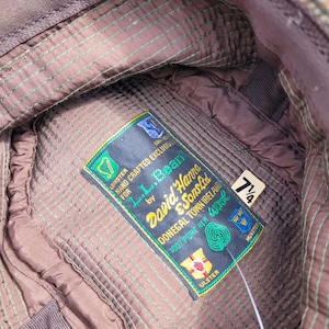 Może przedstawiać: Wnętrze czapki z tweedu z brązową pikowaną podszewką i zielonymi szwami. Prostokątna metka zawiera napis: L.L.Bean by David Hanna & Sons Ltd, Donegal Town Ireland, 100% Pure New Wool. Mała biała metka wskazuje rozmiar 7 1/4.