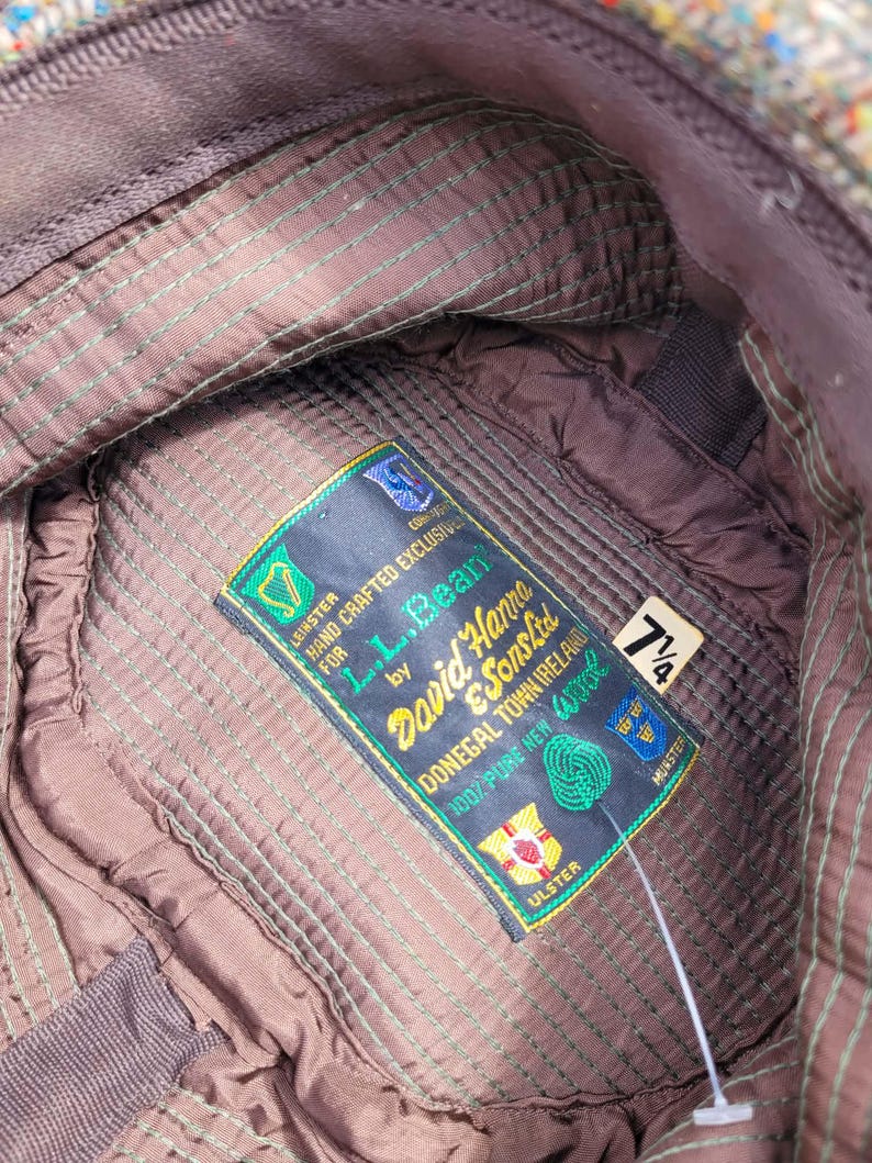 Może przedstawiać: Wnętrze czapki z tweedu z brązową pikowaną podszewką i zielonymi szwami. Prostokątna metka zawiera napis: L.L.Bean by David Hanna & Sons Ltd, Donegal Town Ireland, 100% Pure New Wool. Mała biała metka wskazuje rozmiar 7 1/4.
