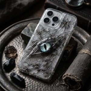 Könnte beinhalten: Transparente Handyhülle mit grauem Marmormuster und blauem Augendesign. Die Hülle hat eine strukturierte Oberfläche und einen transparenten Rand, der die Kamera und die Funktionen des Telefons zeigt. Das Augendesign ist detailliert.