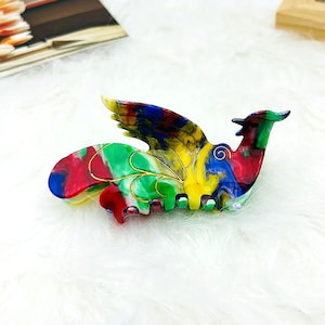 Peut inclure: Une pince &agrave; cheveux en plastique color&eacute;e en forme d'oiseau avec les ailes d&eacute;ploy&eacute;es. La pince est d&eacute;cor&eacute;e de volutes de peinture rouge, jaune, verte, bleue et dor&eacute;e.