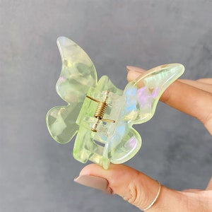 May include: A light green butterfly hair clip with iridescent glitter accents. The clip has a spring-loaded mechanism for holding hair.