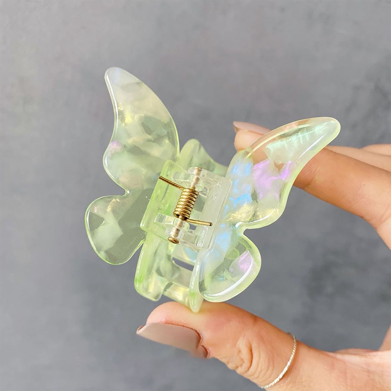 May include: A light green butterfly hair clip with iridescent glitter accents. The clip has a spring-loaded mechanism for holding hair.