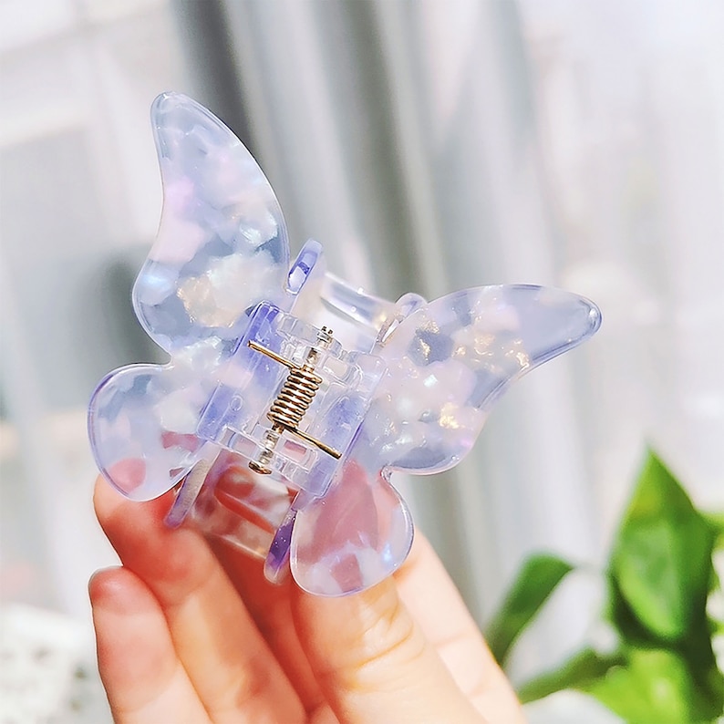 May include: A clear plastic butterfly hair clip with a glittery finish. The clip is open and ready to be used.