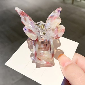 May include: A clear plastic butterfly hair clip with pink, white, and blue marbled accents. The clip has a spring mechanism to hold hair in place.